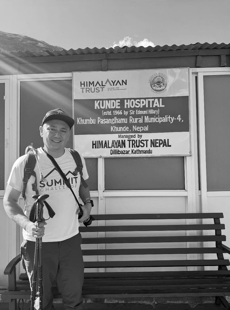 Black-and-white photo of David outside Khunde Hospital, under a Himalayan Trust Nepal sign